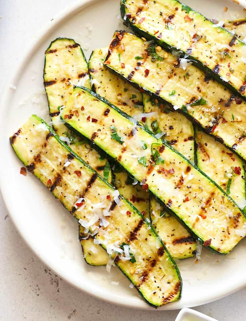 Freshly grilled zucchini on a white platter waiting to be sprinkled with Parmesan and devoured.