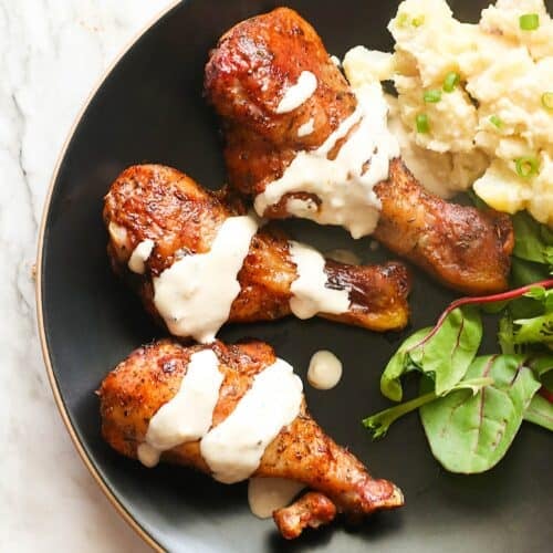 Drizzling juicy, tender smoked chicken legs with homemade white BBQ sauce and potato salad on the side.