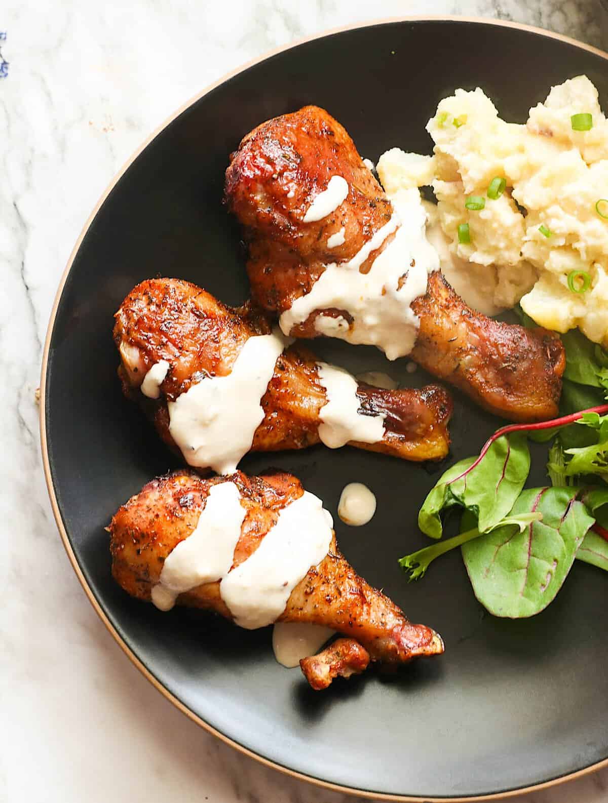 Drizzling juicy, tender smoked chicken legs with homemade white BBQ sauce and potato salad on the side.