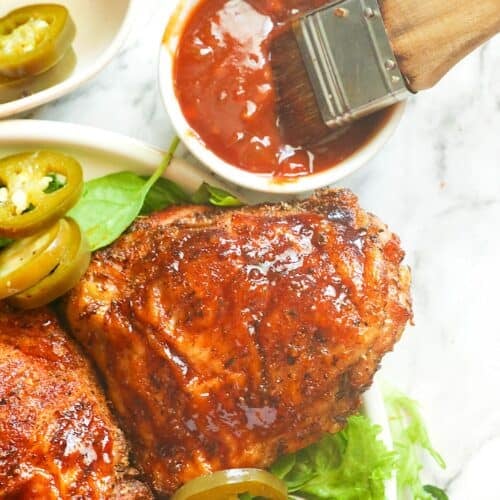 Brushing freshly smoked chicken thighs with BBQ sauce and serving them with pickled jalapenos on a bed of lettuce.