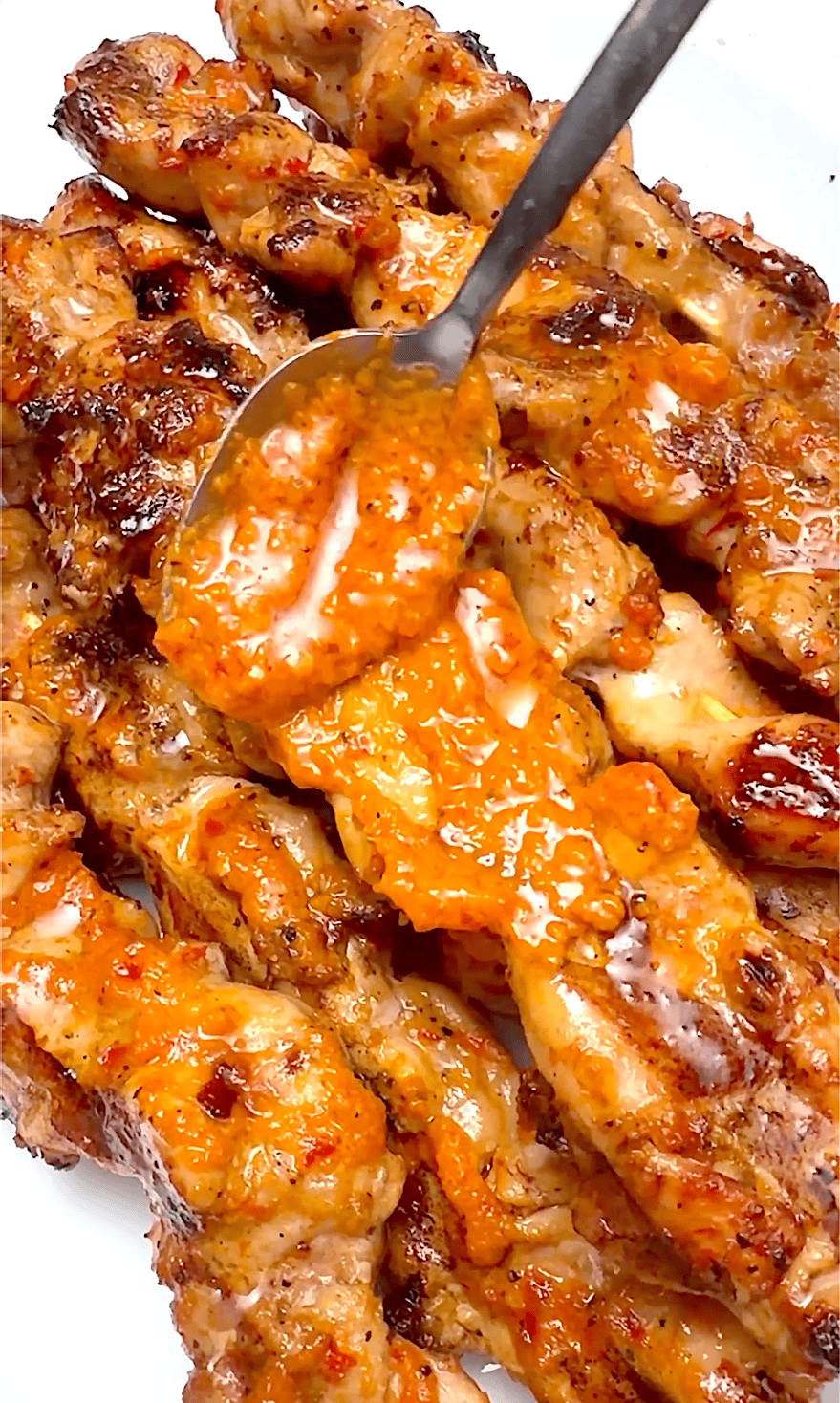 Drizzling more peri peri sauce on grilled chicken skewers.