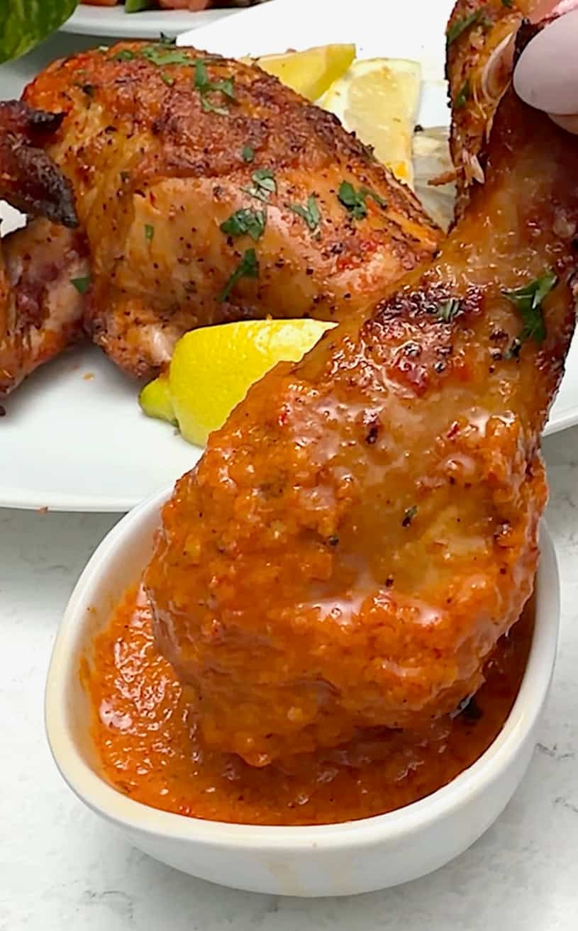 Dipping a grilled chicken leg into a fresh batch of peri peri sauce.