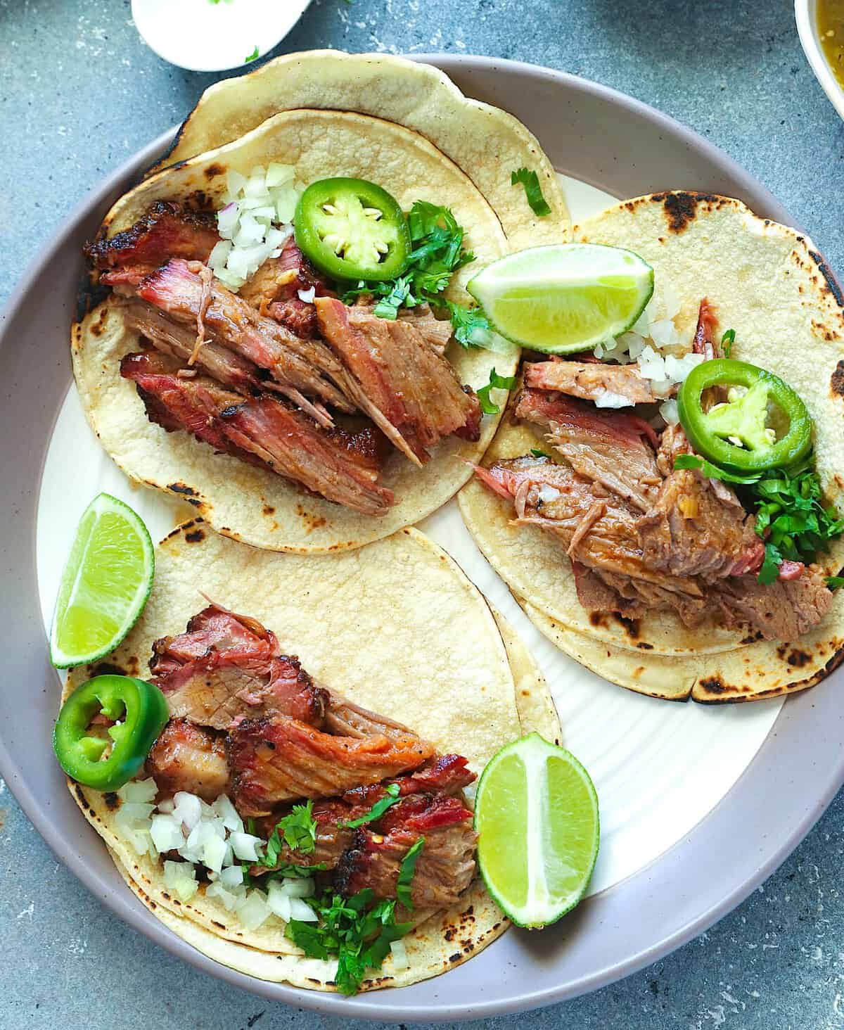 Assembling the tacos with smoked brisket, jalapeños, cilantro, and lime wedges.