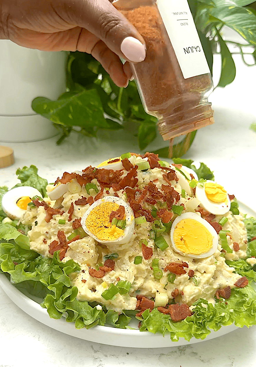 Sprinkling extra Creole seasoning on a garnished potato salad.
