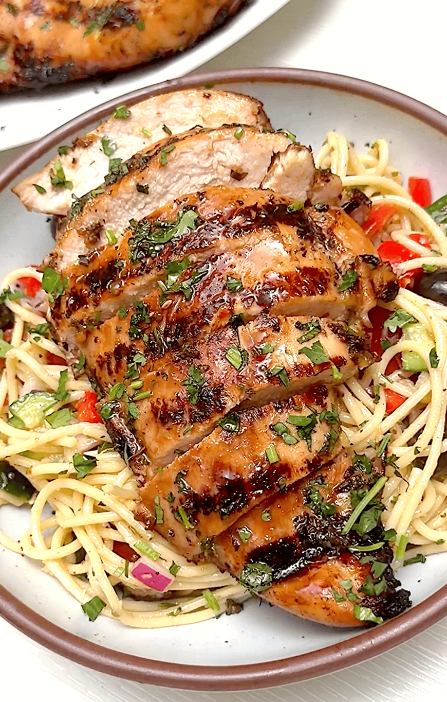 Topping a spaghetti salad with tender, freshly grilled chicken.