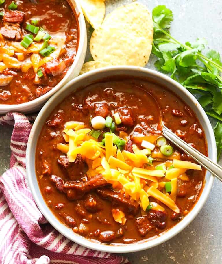Enjoying a comforting, hot bowl of smoked brisket chili topped with grated cheese and sliced green onions.